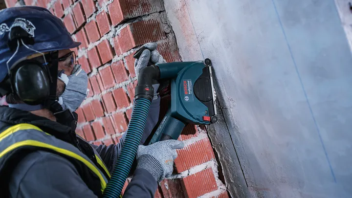 Une personne portant un équipement de sécurité utilise un outil électrique pour meuler un mur en béton.