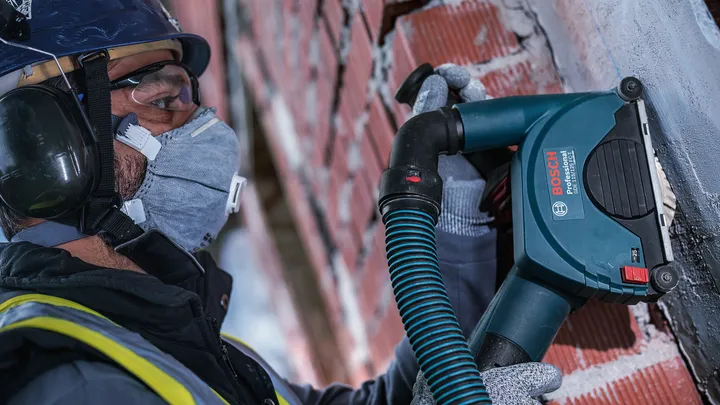 Une personne portant un équipement de sécurité perce une rainure dans un mur de briques à l'aide d'un outil électrique.