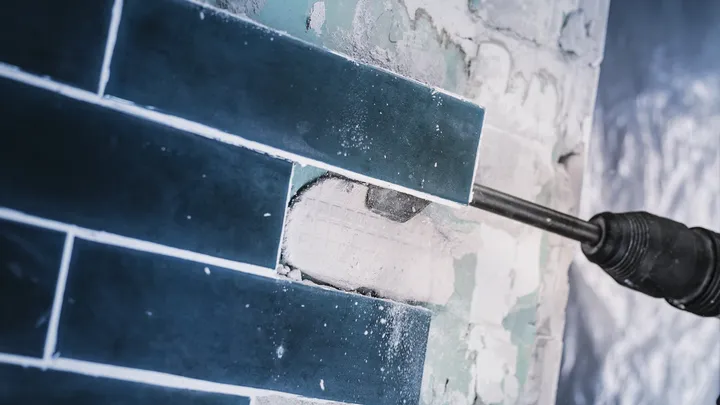 Un outil électrique ébrèche des carreaux bleus d'un mur.