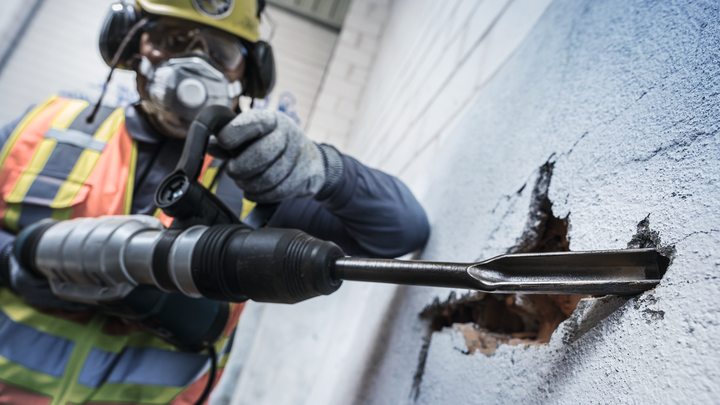 Une personne portant un équipement de sécurité utilise un marteau perforateur pour percer un mur en béton.