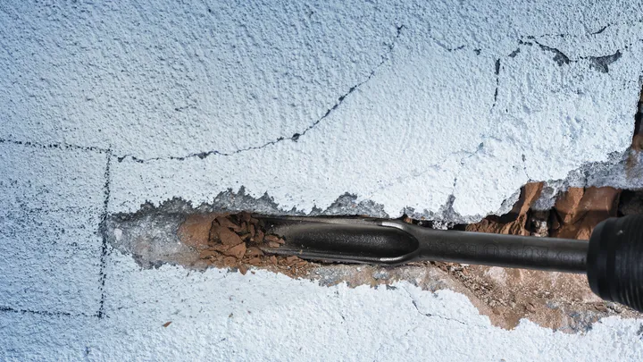 Ciseau démolissant un mur de béton fissuré.