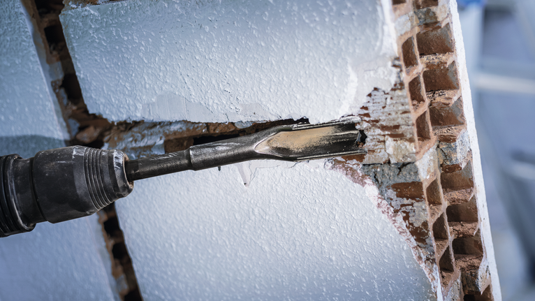 Un marteau perforateur perce un trou dans un mur de briques blanches.