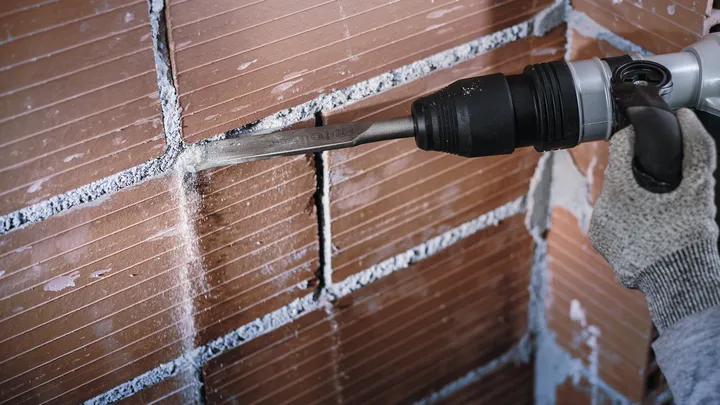 Une personne portant un équipement de sécurité utilise un ciseau électrique pour retirer le mortier d'un mur de briques.