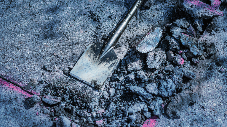 Un burin brise l'asphalte en gravats sur une surface de construction marquée.