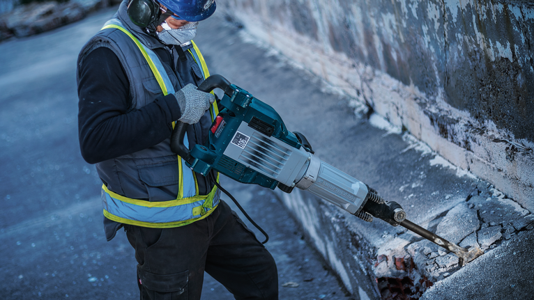 Une personne portant un équipement de sécurité utilise un marteau de démolition pour briser le béton.