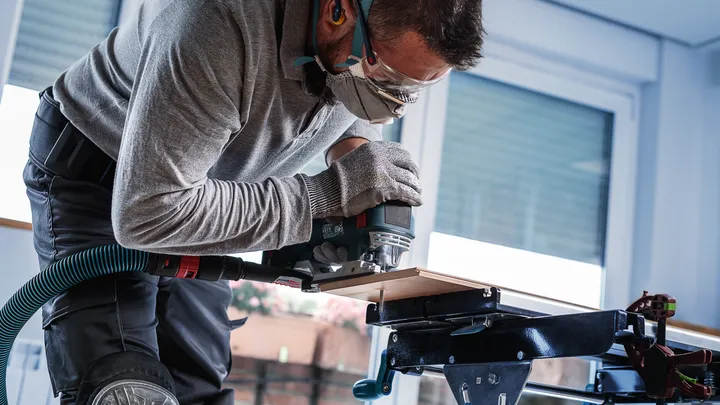 Une personne portant un équipement de sécurité utilise un outil électrique pour couper une planche de bois.