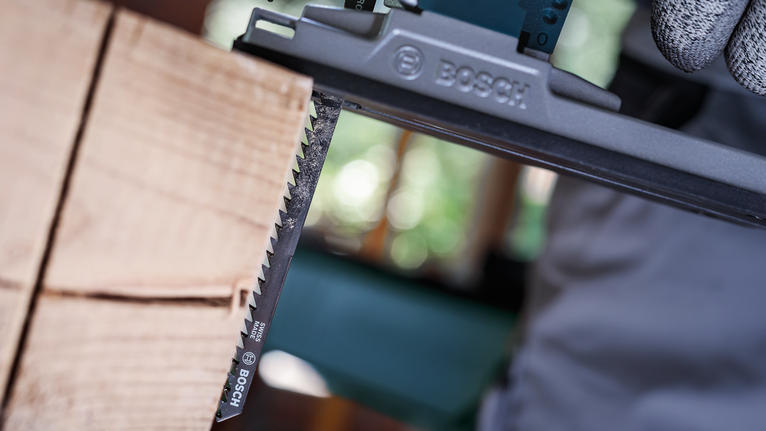 Une personne portant un équipement de sécurité utilise une scie alternative pour couper du bois.