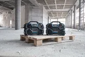 Deux radios de chantier robustes placées sur une palette en bois dans une structure partiellement construite.