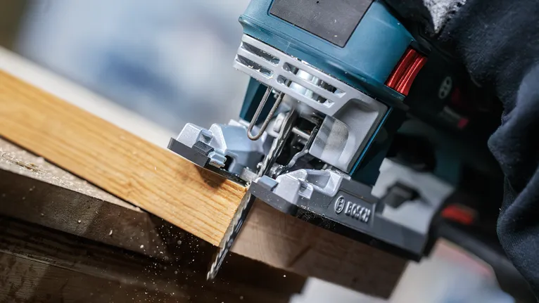 Une personne portant un équipement de sécurité utilise une scie sauteuse pour couper une planche de bois.