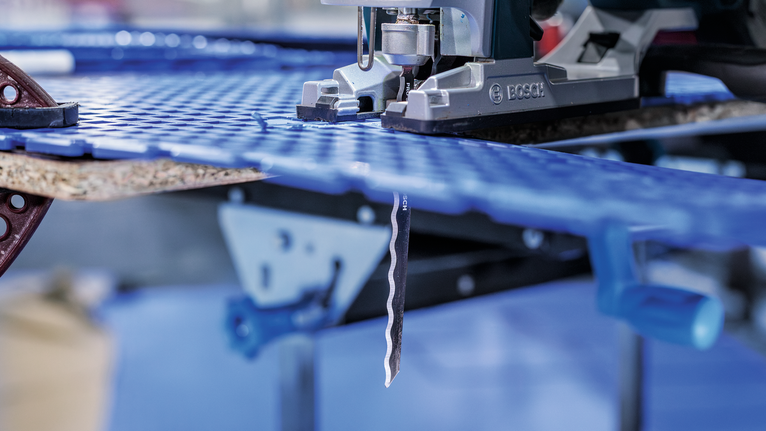 Scie sauteuse découpant une feuille de plastique bleu dans un atelier.