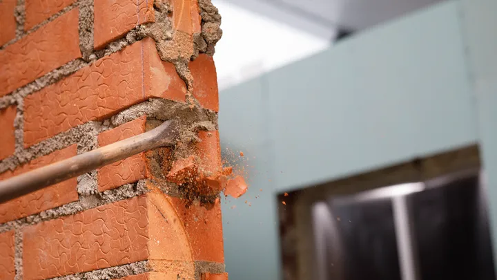 Outil de ciseau perçant un mur de briques rouges lors de la démolition.