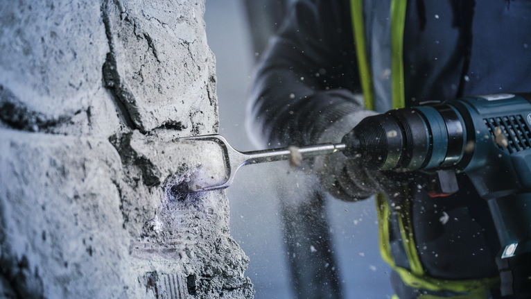 Une personne portant un équipement de sécurité utilise un marteau perforateur pour briser le béton.