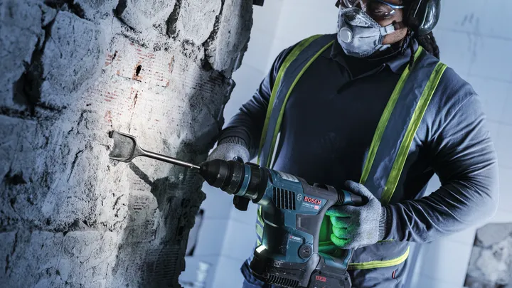 Un ouvrier portant un équipement de sécurité utilise un marteau perforateur pour ciseler un mur en béton.