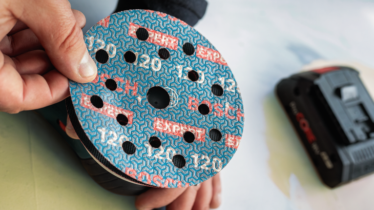 Une personne fixe un disque de ponçage à une ponceuse électrique.