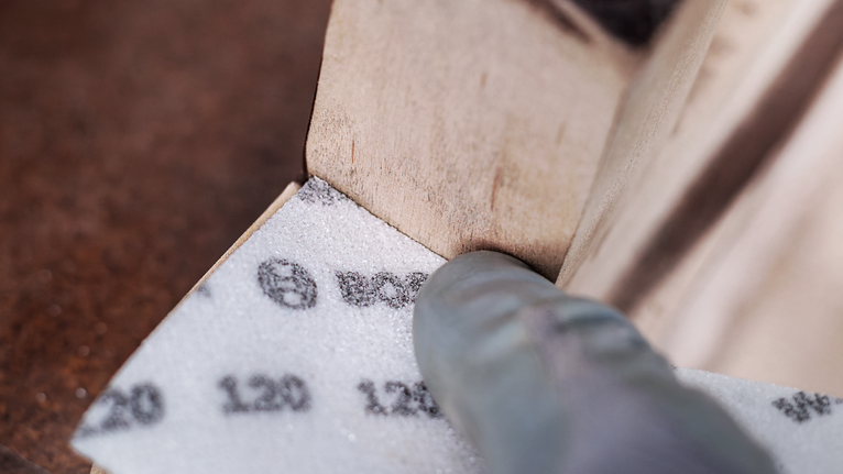 Personne portant un équipement de sécurité ponçant le coin d'une surface en bois.