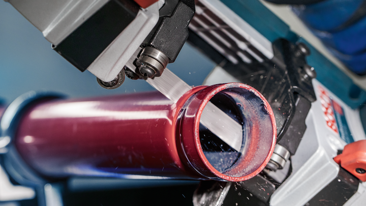 Scie à métaux coupant un tuyau rouge, créant de fins copeaux de métal.