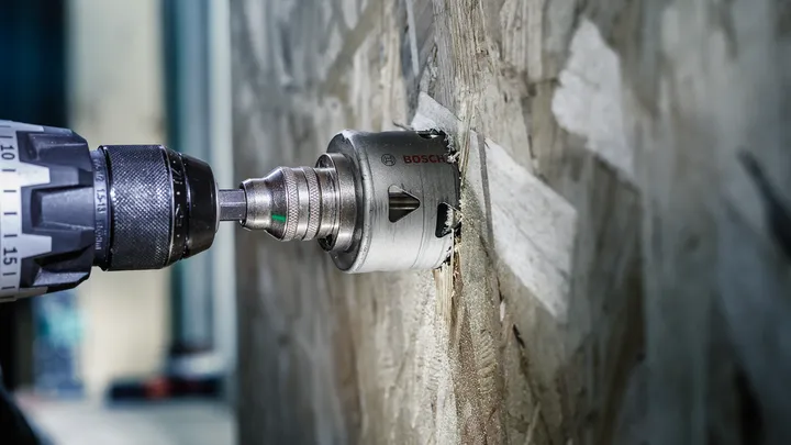 Perceuse électrique avec scie cloche découpant un mur en bois.