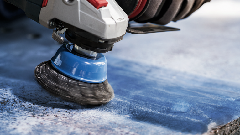 Une personne portant un équipement de sécurité polit une surface bleue avec un outil à brosse rotative.