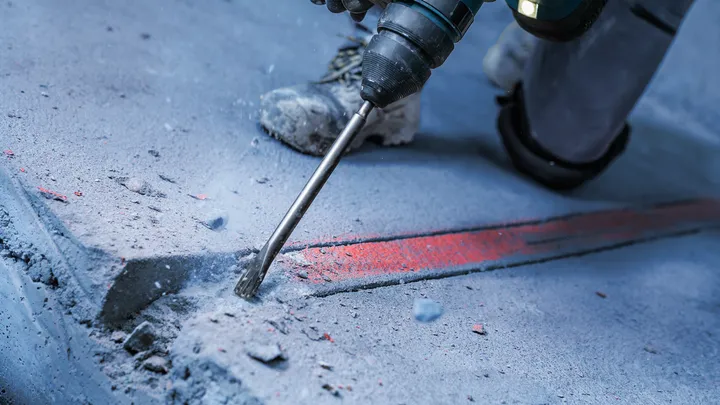 Une personne portant un équipement de sécurité utilise un marteau perforateur pour briser le béton.
