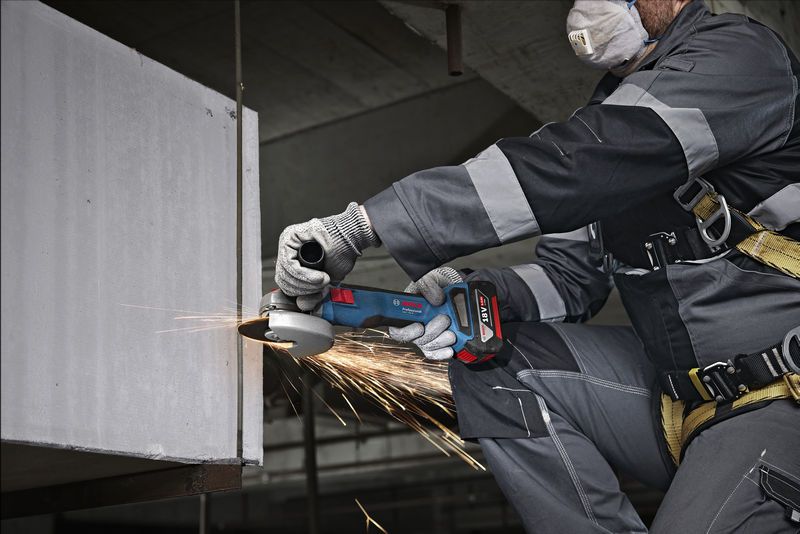 Une personne portant un équipement de sécurité meule un bord en béton avec une meuleuse d'angle.