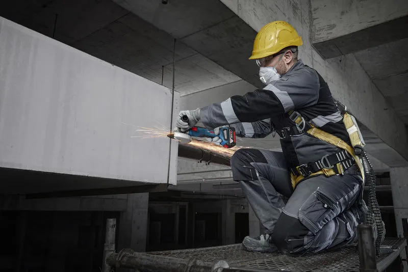 Une personne portant un équipement de sécurité broie du béton avec un outil électrique sur un chantier de construction.