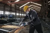 Une personne portant un équipement de sécurité broie du métal, produisant des étincelles brillantes dans une usine.