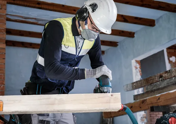 Une personne portant un équipement de sécurité ponce une poutre en bois avec un outil électrique.