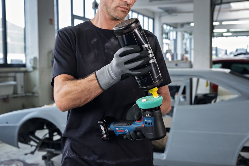 Une personne portant un équipement de sécurité applique du produit à polir sur une polisseuse dans un atelier automobile.