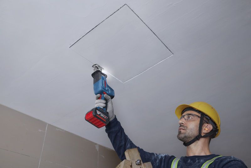 Une personne portant un équipement de sécurité coupe un panneau de plafond avec une scie alternative.