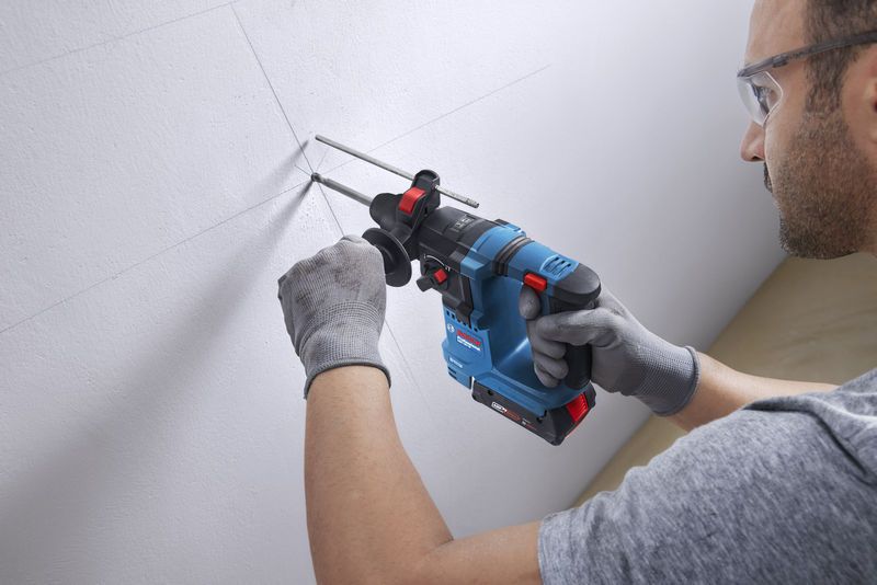 Une personne portant un équipement de sécurité perce un mur avec un marteau perforateur.