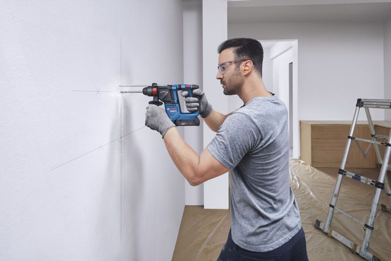 Une personne portant un équipement de sécurité perce un trou dans un mur blanc marqué.