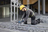 Une personne portant un équipement de sécurité serre des boulons sur un cadre métallique avec une clé à cliquet sans fil.
