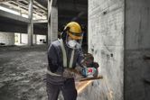 Une personne portant un équipement de sécurité meule un mur en béton avec une meuleuse d'angle, produisant des étincelles.