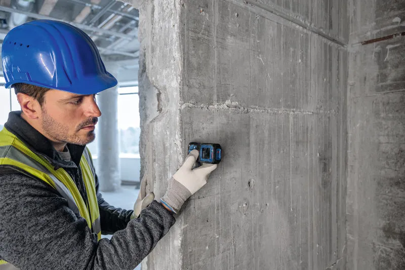 Une personne portant un équipement de sécurité utilise un télémètre laser contre un mur en béton.