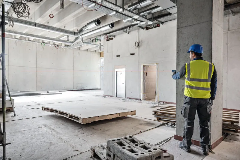 Une personne portant un équipement de sécurité utilise un télémètre laser dans un grand bâtiment en construction.