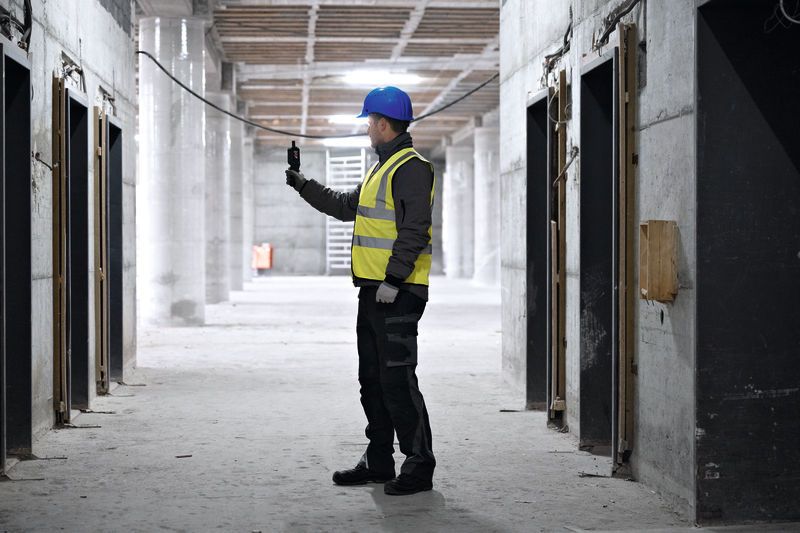 Une personne portant un équipement de sécurité vérifie un thermo-hygromètre à l'intérieur d'un chantier de construction.