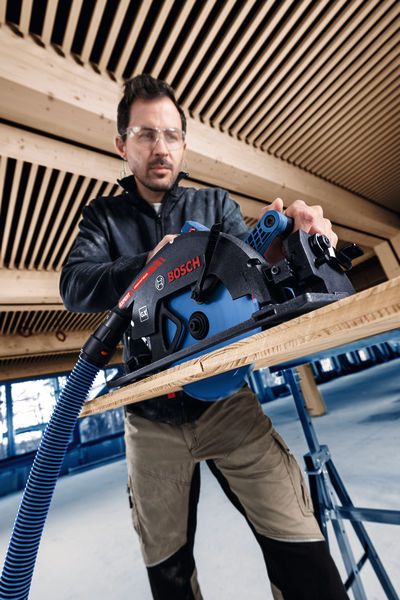 Une personne portant un équipement de sécurité utilise une scie circulaire sans fil pour couper du bois.