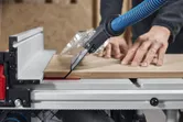 Une personne guide le bois à travers une scie à table équipée d'un système d'extraction de poussière.