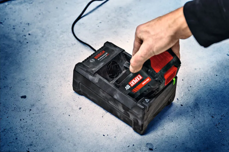 Une personne insère une batterie d’outil sans fil dans une station de charge sur un sol en béton.