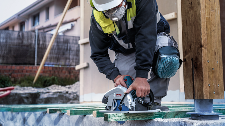 Une personne portant un équipement de sécurité coupe du bois avec une scie circulaire sur un chantier de construction.