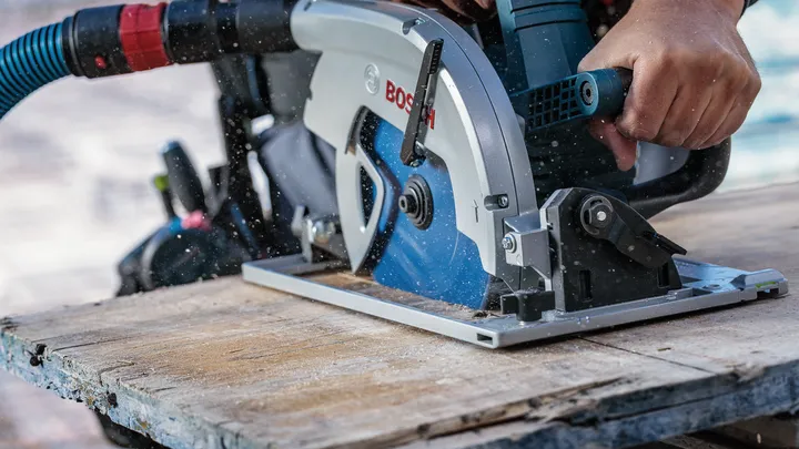 Une personne portant un équipement de sécurité utilise une scie circulaire pour couper une planche de bois.