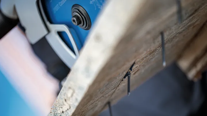 Scie circulaire coupant une planche de bois avec des clous métalliques qui dépassent.