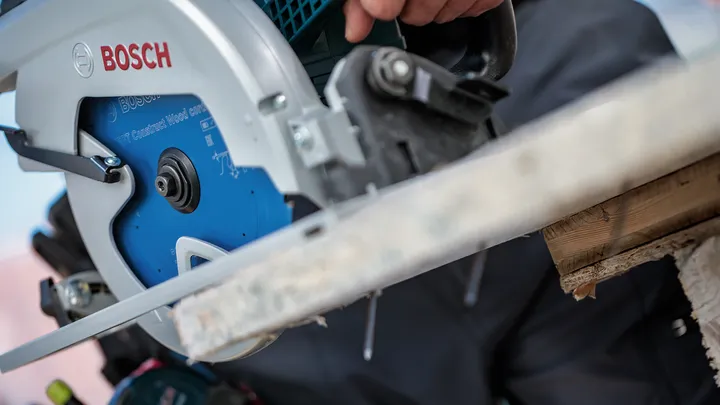 Une personne portant un équipement de sécurité utilise une scie circulaire pour couper une planche de bois.