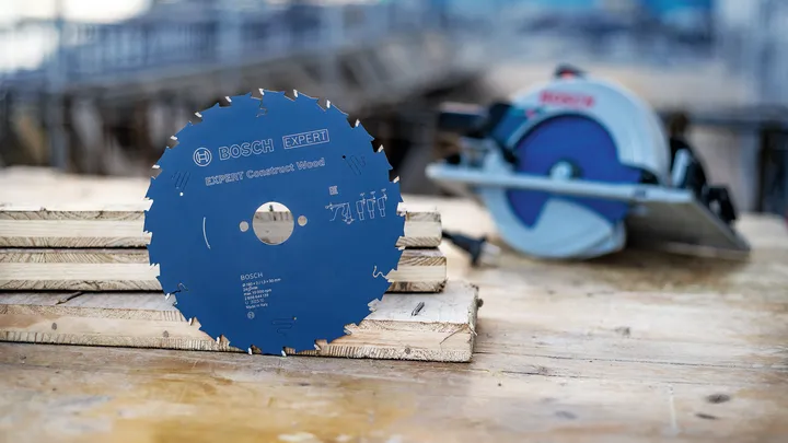 Lame de scie circulaire posée sur du bois empilé près d'une scie électrique sur un chantier de construction.