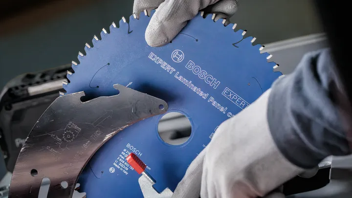 Une personne portant un équipement de sécurité installe une lame de scie circulaire sur une machine.