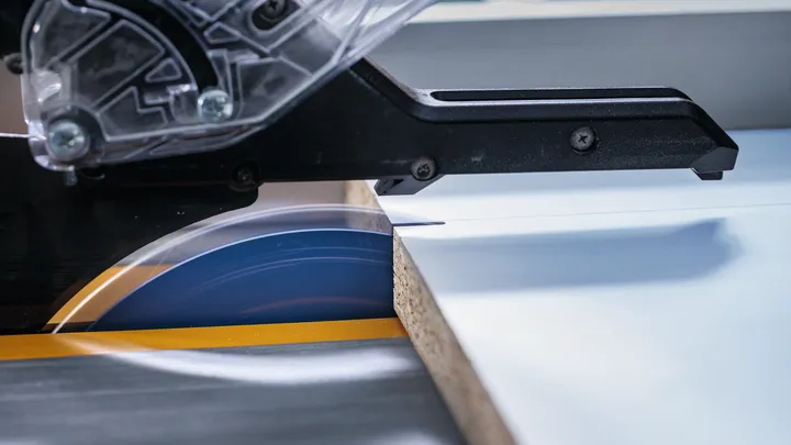 Scie circulaire coupant une planche de bois stratifiée sur un établi.