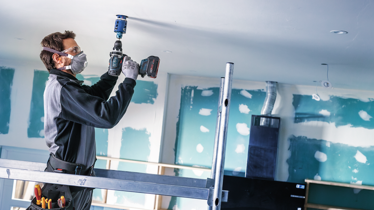 Une personne portant un équipement de sécurité perce un trou dans un plafond sur un chantier de construction.