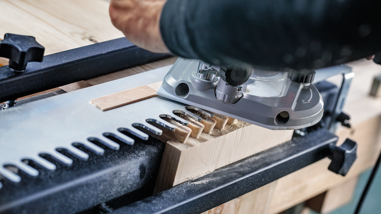 Une personne utilise un outil électrique pour couper des joints en queue d’aronde dans une planche de bois.