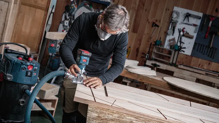 Une personne portant un équipement de sécurité utilise un outil électrique pour creuser des rainures dans une planche de bois.