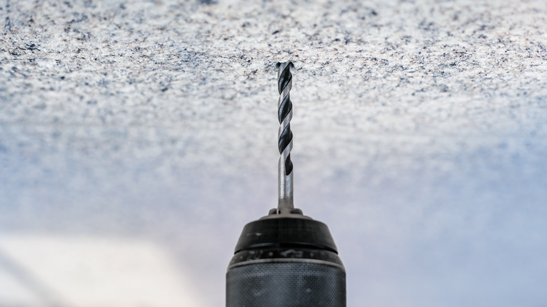 Perceuse sans fil perçant un trou dans un plafond en béton.
